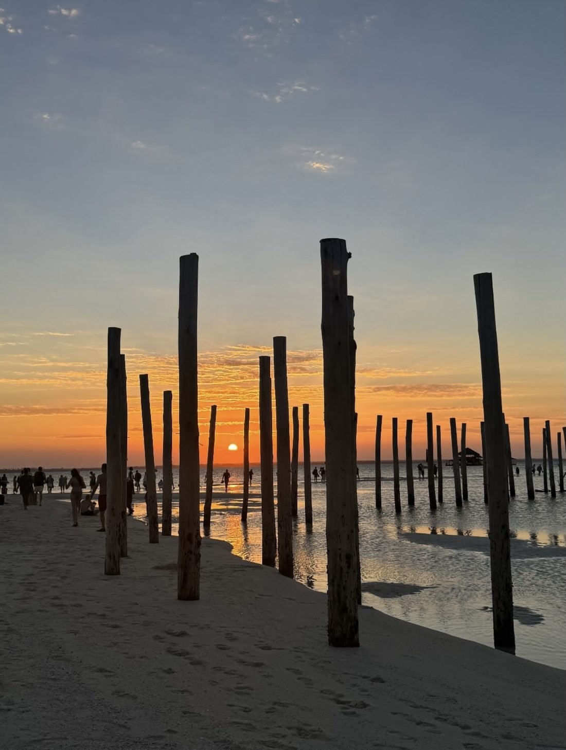 The sun setting over the shallows between weathered wooden posts