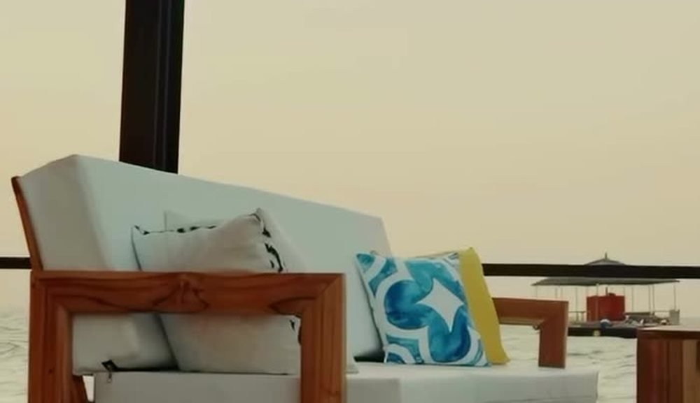 A white sofa with blue and yellow cushions on the deck at sunset