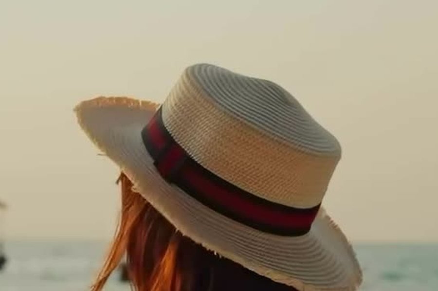 A guest in a straw hat looking out over the sea at dusk